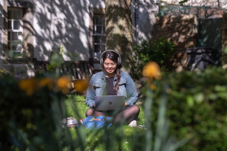 A student sitting outside with a laptop